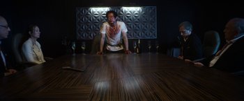 Movie still from “Mayhem” (2017), directed by Joe Lynch – A man sitting at a wooden table with wine glasses; Medium shot, Low angle