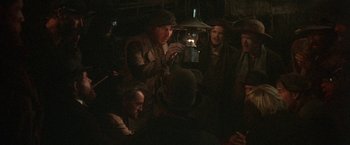 Movie still from “McCabe & Mrs. Miller” (1971), directed by Robert Altman – A group of people gathered around a man holding a lantern; Medium shot, High angle