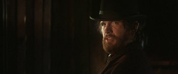 Movie still from “McCabe & Mrs. Miller” (1971), directed by Robert Altman – A man with a beard wearing a black hat; Close Up shot, Over the shoulder angle