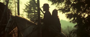 Movie still from “McCabe & Mrs. Miller” (1971), directed by Robert Altman – A man and a woman riding a horse through the woods; Wide shot, Low angle