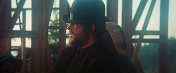 Movie still from “McCabe & Mrs. Miller” (1971), directed by Robert Altman – A man with a beard wearing a black hat; Close Up shot, Over the shoulder angle