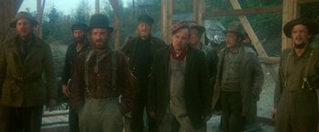 Movie still from “McCabe & Mrs. Miller” (1971), directed by Robert Altman – A group of men standing next to each other in front of a building; Medium shot, Low angle