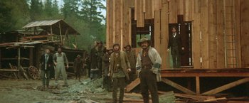 Movie still from “McCabe & Mrs. Miller” (1971), directed by Robert Altman – A group of men standing in front of a wooden building; Wide shot, Low angle