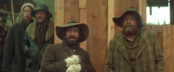 Movie still from “McCabe & Mrs. Miller” (1971), directed by Robert Altman – A man in a hat is holding a glove; Medium shot, Low angle