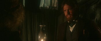 Movie still from “McCabe & Mrs. Miller” (1971), directed by Robert Altman – A man in a suit and tie standing next to an oil lamp; Close Up shot, Over the shoulder angle