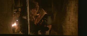 Movie still from “McCabe & Mrs. Miller” (1971), directed by Robert Altman – A woman is reading a book in the dark; Medium shot, High angle