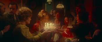 Movie still from “McCabe & Mrs. Miller” (1971), directed by Robert Altman – A group of people standing around a birthday cake; Medium shot, High angle