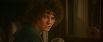 Movie still from “McCabe & Mrs. Miller” (1971), directed by Robert Altman – A man with a curly hair and a blue shirt is posing for a picture; Close Up shot, Over the shoulder angle