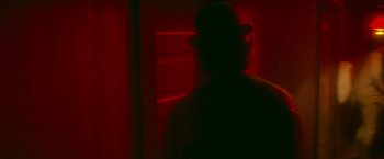 Movie still from “McCabe & Mrs. Miller” (1971), directed by Robert Altman – A man wearing a hat standing next to a red wall; Close Up shot, Over the shoulder angle