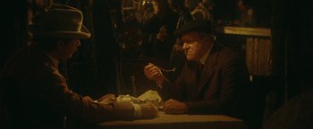 Movie still from “McCabe & Mrs. Miller” (1971), directed by Robert Altman – An older man sitting at a table eating a sandwich; Medium shot, Over the shoulder angle
