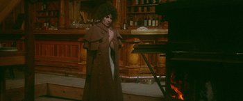 Movie still from “McCabe & Mrs. Miller” (1971), directed by Robert Altman – A woman in a brown coat standing in front of a bar; Medium shot, High angle