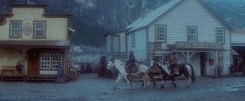 Movie still from “McCabe & Mrs. Miller” (1971), directed by Robert Altman – A group of people riding horses in front of a house; Extreme Wide shot, Low angle