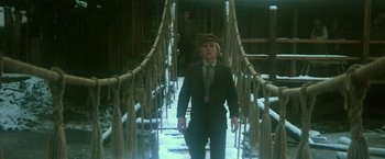 Movie still from “McCabe & Mrs. Miller” (1971), directed by Robert Altman – A man walking across a rope bridge with a hat on; Medium shot, High angle