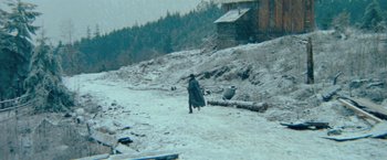 Movie still from “McCabe & Mrs. Miller” (1971), directed by Robert Altman – A man walking in the snow near a log house; Extreme Wide shot, High angle