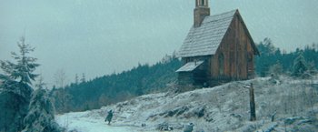 Movie still from “McCabe & Mrs. Miller” (1971), directed by Robert Altman – A person is walking in the snow near a house; Extreme Wide shot, Low angle