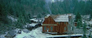 Movie still from “McCabe & Mrs. Miller” (1971), directed by Robert Altman – An image of a building in the middle of a snow covered forest; Extreme Wide shot, High angle