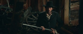 Movie still from “McCabe & Mrs. Miller” (1971), directed by Robert Altman – A man in a suit and hat holding a sword; Medium shot, Low angle