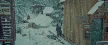 Movie still from “McCabe & Mrs. Miller” (1971), directed by Robert Altman – A man walking in the snow next to a wooden structure; Extreme Wide shot, High angle