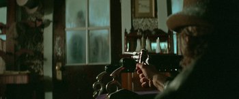Movie still from “McCabe & Mrs. Miller” (1971), directed by Robert Altman – A person holding a gun in a room with a window; Close Up shot, Over the shoulder angle