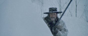 Movie still from “McCabe & Mrs. Miller” (1971), directed by Robert Altman – A man with a long beard holding an umbrella in the snow; Medium shot, Low angle