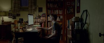 Movie still from “Me and Earl and the Dying Girl” (2015), directed by Alfonso Gomez-Rejon – A man sitting in front of a computer in a dark room; Medium shot, Over the shoulder angle
