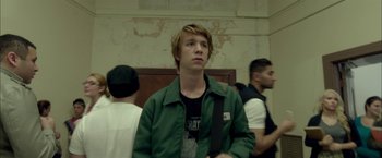 Movie still from “Me and Earl and the Dying Girl” (2015), directed by Alfonso Gomez-Rejon – A man in a green jacket standing next to other people; Medium shot, Low angle