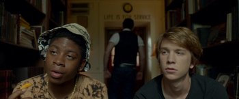 Movie still from “Me and Earl and the Dying Girl” (2015), directed by Alfonso Gomez-Rejon – Two people sitting in front of a door way; Close Up shot, Over the shoulder angle