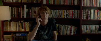 Movie still from “Me and Earl and the Dying Girl” (2015), directed by Alfonso Gomez-Rejon – A man sitting in front of a book shelf talking on a cell phone; Medium shot, Over the shoulder angle