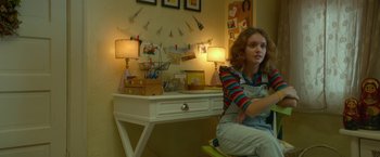 Movie still from “Me and Earl and the Dying Girl” (2015), directed by Alfonso Gomez-Rejon – A girl sitting in front of a white desk with many pictures on the wall; Medium shot, Low angle