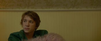 Movie still from “Me and Earl and the Dying Girl” (2015), directed by Alfonso Gomez-Rejon – A man sitting in front of a wall with a pink feather boa; Close Up shot, Over the shoulder angle