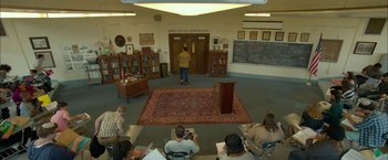 Movie still from “Me and Earl and the Dying Girl” (2015), directed by Alfonso Gomez-Rejon – A group of people sitting in a room with a podium; Extreme Wide shot, High angle