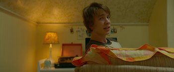 Movie still from “Me and Earl and the Dying Girl” (2015), directed by Alfonso Gomez-Rejon – A man sitting on top of a couch in a living room; Medium shot, Over the shoulder angle