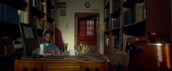 Movie still from “Me and Earl and the Dying Girl” (2015), directed by Alfonso Gomez-Rejon – A person sitting at a desk in a room with many books; Wide shot, Low angle