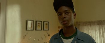 Movie still from “Me and Earl and the Dying Girl” (2015), directed by Alfonso Gomez-Rejon – A young man wearing a baseball cap in front of a wall of pictures; Close Up shot, Low angle