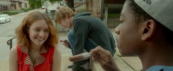 Movie still from “Me and Earl and the Dying Girl” (2015), directed by Alfonso Gomez-Rejon – A group of young people sitting on the side of the street; Medium shot, Over the shoulder angle