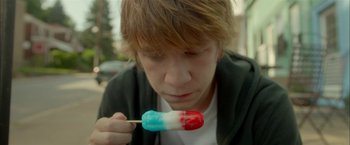 Movie still from “Me and Earl and the Dying Girl” (2015), directed by Alfonso Gomez-Rejon – A young man eating a red , white , and blue treat; Close Up shot, High angle