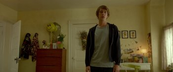 Movie still from “Me and Earl and the Dying Girl” (2015), directed by Alfonso Gomez-Rejon – A young man standing in a living room; Medium shot, Low angle