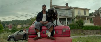 Movie still from “Me and Earl and the Dying Girl” (2015), directed by Alfonso Gomez-Rejon – A man sitting on the back of a red truck with a dog; Medium shot, Low angle