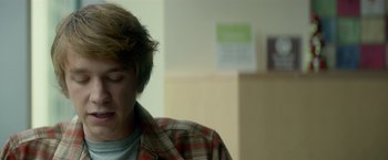 Movie still from “Me and Earl and the Dying Girl” (2015), directed by Alfonso Gomez-Rejon – A young man in a plaid shirt is looking down; Close Up shot, Over the shoulder angle