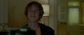 Movie still from “Me and Earl and the Dying Girl” (2015), directed by Alfonso Gomez-Rejon – A young man smiling for the camera in front of a lamp; Close Up shot, Over the shoulder angle