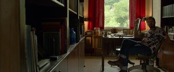 Movie still from “Me and Earl and the Dying Girl” (2015), directed by Alfonso Gomez-Rejon – A man sitting in a room next to a bookshelf; Wide shot, Low angle