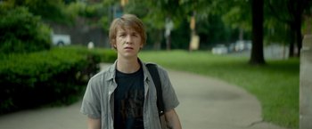 Movie still from “Me and Earl and the Dying Girl” (2015), directed by Alfonso Gomez-Rejon – A young man standing on a sidewalk with a backpack; Medium shot, Over the shoulder angle