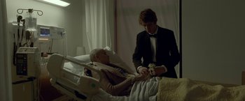 Movie still from “Me and Earl and the Dying Girl” (2015), directed by Alfonso Gomez-Rejon – A man in a suit and a bow tie standing next to an older man in a hospital bed; Medium shot, Over the shoulder angle