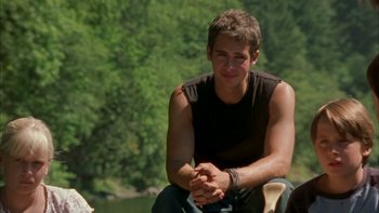 Movie still from “Mean Creek” (2004), directed by Jacob Estes – A young man sitting on a chair in front of a body of water; Medium shot, Over the shoulder angle