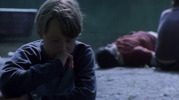 Movie still from “Mean Creek” (2004), directed by Jacob Estes – A young boy sitting on the ground next to a dead body; Medium shot, High angle
