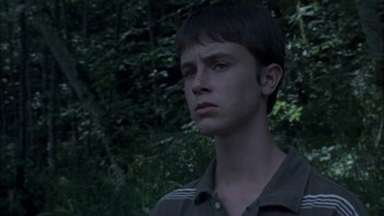 Movie still from “Mean Creek” (2004), directed by Jacob Estes – A young man is standing in front of a forest; Close Up shot, Low angle