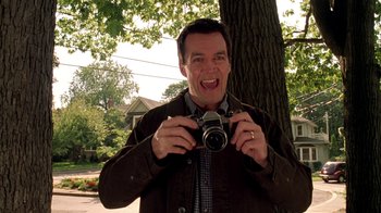 Movie still from “Mean Girls” (2004), directed by Mark Waters – A man holding a camera in front of a tree; Medium shot, Low angle