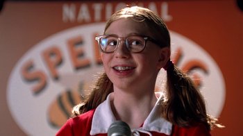 Movie still from “Mean Girls” (2004), directed by Mark Waters – A young girl wearing glasses and a red shirt is talking into a microphone; Close Up shot, Low angle