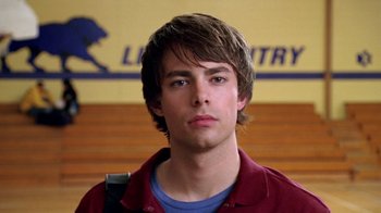 Movie still from “Mean Girls” (2004), directed by Mark Waters – A young man with long brown hair wearing a red shirt; Close Up shot, Low angle