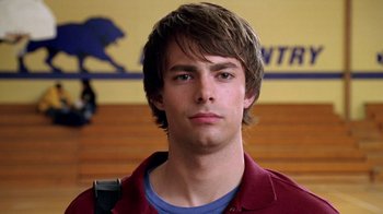 Movie still from “Mean Girls” (2004), directed by Mark Waters – A young man with long brown hair wearing a red shirt; Close Up shot, Low angle